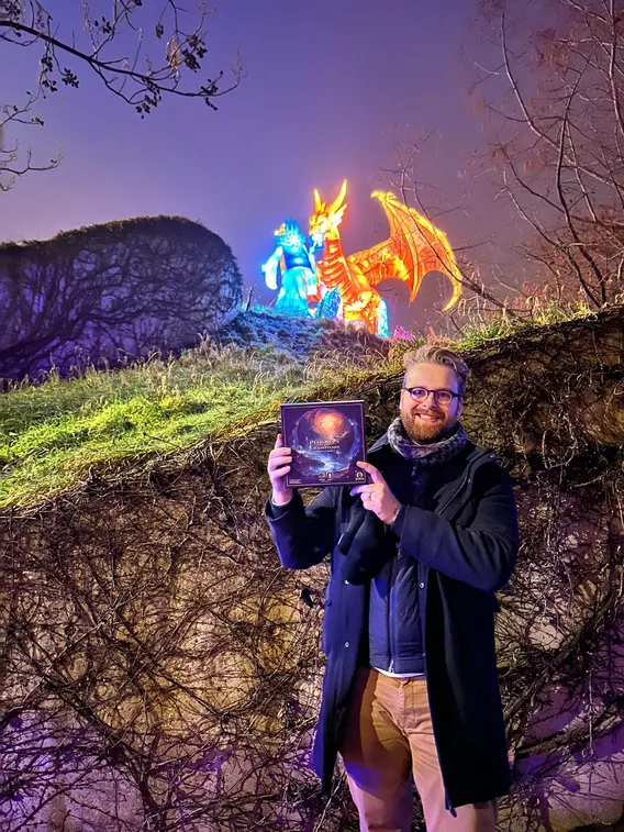 Maker houdt de doos van Portals & Champions omhoog bij verlichte drakenfiguren